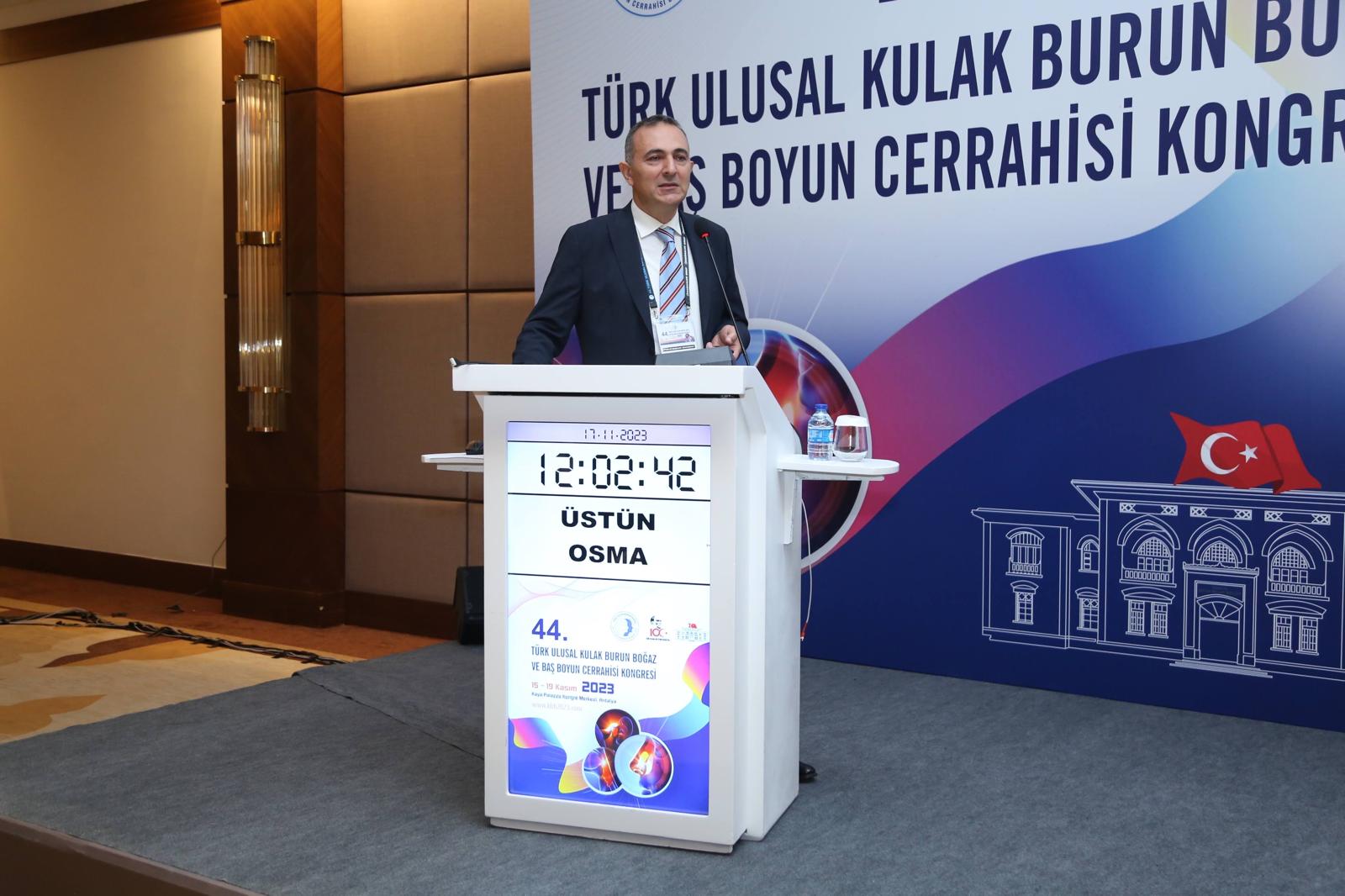 A presenter speaks at the 44th Turkish National Otorhinolaryngology and Head Neck Surgery Congress, with a podium display showcasing the event details.
